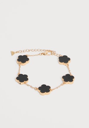 Bracelet chaîne en or avec cinq breloques noires en forme de trèfle à quatre feuilles et fermeture mousqueton sur fond blanc.