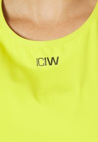 Zbliżenie na osobę w jasnoniebieskiej koszulce z czarnym napisem "ICIW" poniżej dekoltu.