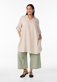 Tunic in lino beige con scollo a V, maniche arrotolate e una tasca. Abbinato a culotte in lino verde chiaro, larghi, e sandali neri con cinturini.