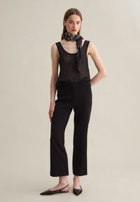 Black mesh tank top with a scoop neckline, paired with black tailored pants and black flat shoes. Accented with a patterned black scarf.