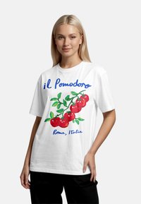Bílý bavlněný tričko s barevným grafikou rajčete a zelenými listy, text "il Pomodoro" a "Roma, Italia" v modré barvě. Volný střih.