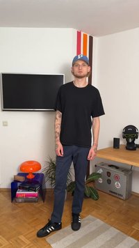 Black short-sleeve T-shirt, navy blue pants, and black sneakers with white stripes. Tattooed arms visible. Simple and casual attire.