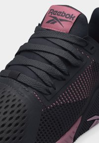 Μαύρο και ροζ αθλητικό παπούτσι Reebok με υφασμάτινο επάνω μέρος με υφή, χοντρά μαύρα κορδόνια και ροζ ετικέτα γλώσσας με το λογότυπο.