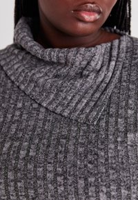 Un pull gris à col cheminée présentant des rayures verticales texturées. Fabriqué en matériau doux avec un motif côtelé et une coupe décontractée.