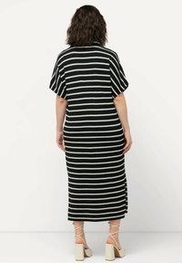 Robe rayée noir et blanc avec des manches courtes, longueur mi-mollet, tissu texturé, fentes latérales, associée à des sandales à talons carrés beiges.