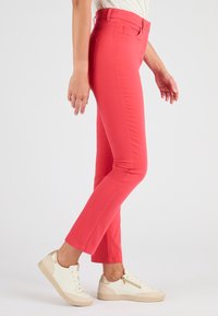 Getailleerde koraalkleurige broek van rekbare katoenmix, met een middelhoge taille, vijf zakken en gecombineerd met beige vetersneakers.