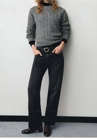 Grauer gestrickter Pullover mit strukturiertem Muster und verzierten Schultern, kombiniert mit hoch taillierten schwarzen Jeans und schwarzen Slippern.