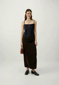 Ναυτικό μπλε αμάνικο τοπ με κουμπιά, συνδυασμένο με έναν σκούρο καφέ μακρύ φούστα. Το μοντέλο κρατά μια μικρή καφέ τσάντα χειρός και φοράει μαύρες λούφες.