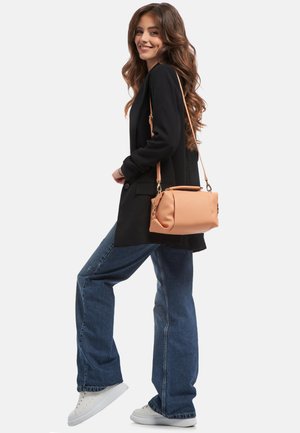 Tan faux læder skuldertaske med en struktureret form, top-håndtag og aftagelig rem. Båret med en sort blazer og flagrende denimjeans.