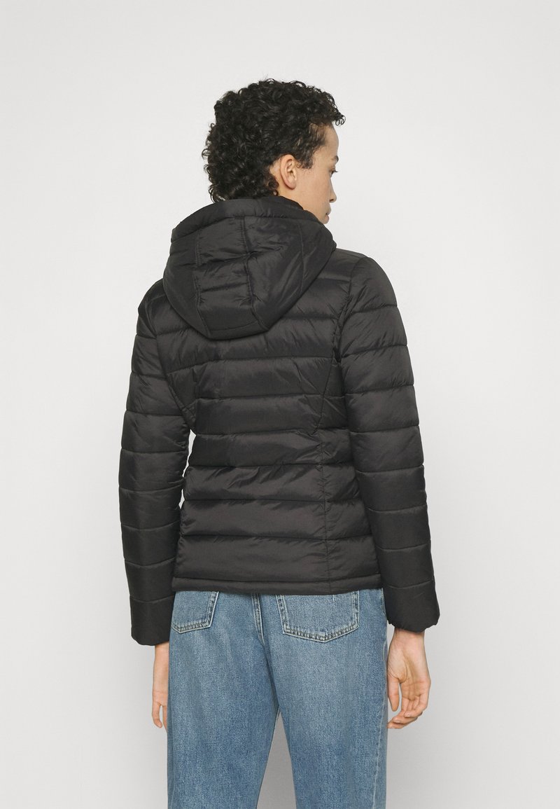 Chaqueta de plumas negra con capucha, con textura acolchada horizontal. El material parece brillante. Combinada con jeans de tiro alto en azul claro.