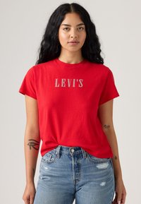 Rød bomull t-skjorte med rund hals og korte ermer med "LEVI'S" logo i hvitt, parret med lys blå denimjeans.