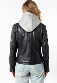 Zwarte leren jack met grijze sweatshirtvoering, met een aansluitend ontwerp, elleboogpatches en drukknopen. Lichte blauwe jeans zichtbaar daaronder.