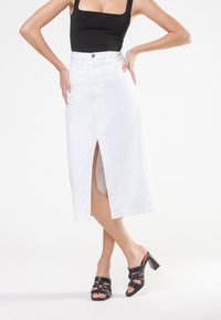 Hvid denim midi-nederdel med slids foran, høj talje og fem-lomme design, parret med sorte blokhæle sandaler.