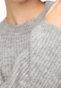 Pull gris tricoté avec une texture côtelée et un col rond, présentant une coupe ample et un tissu doux et duveteux.