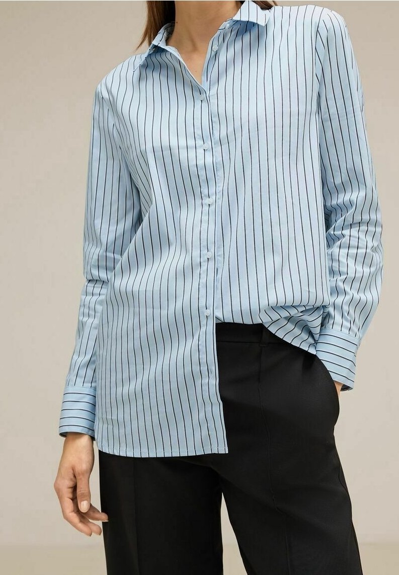 Ljusblå långärmad skjorta med vertikala mörka ränder, knappförslutning fram och mjukt tyg. Stylad med svarta byxor.