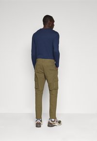 Pantalones cargo en algodón verde oliva, con bolsillos cargo laterales y un corte ajustado, combinados con zapatillas oscuras y una camiseta de manga larga navy.