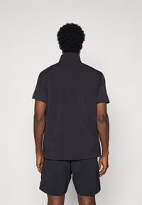 Black short-sleeve athletic shirt with a standing collar, smooth texture, and minimal design. Paired with matching black shorts.