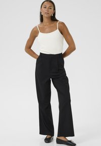 Pantalones negros de cintura alta con pliegues, que cuentan con un diseño de pierna recta. Combinados con una camisola blanca de tela suave y con un hardware mínimo.