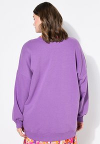 Pull à capuche violet oversize avec un col rond, des épaules tombantes et des poignets côtelés, fabriqué à partir d'un matériau doux.