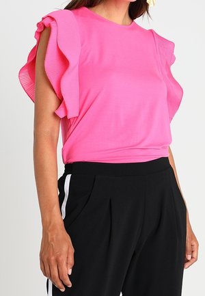 Vaaleanpunainen lyhythihainen paita, jossa on röyhelöillä varustetut ribbihihat. Yhdistetty mustiin housuihin, joissa on valkoiset sivuraitat ja rento istuvuus.