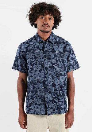 Chemise à manches courtes en tissu bleu marine avec un motif botanique en bleu clair. Modèle boutonné avec col classique et coupe décontractée.