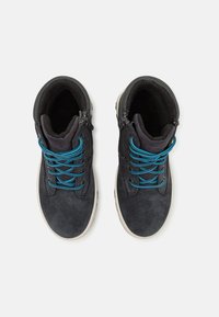 Botas de tobillo de ante negro con cordones azules, con un collar acolchado y suelas de goma blanca. Cremallera en el costado para facilitara la puesta.