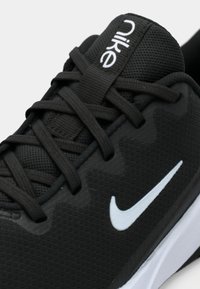 Sort atletiksko med en tekstureret overdel, der har sorte snørebånd, en polstret krave og en hvid Nike swoosh-logo på siden.