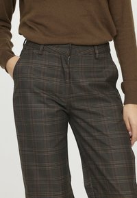 Pantalons à carreaux gris foncé avec de fines lignes orange et blanches. Dotés d'une fermeture éclair sur le devant et de poches latérales, fabriqués à partir d'un tissu lisse.