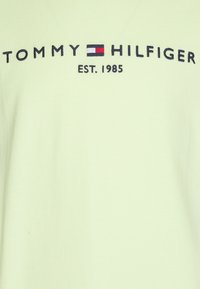 Světle zelené bavlněné tričko s vyšívaným logem "TOMMY HILFIGER" a "EST. 1985" v námořnické modři, s červeným a bílým emblémem.