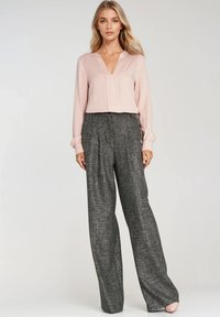 Jasnoróżowa bluzka z dekoltem w kształcie V i długimi rękawami; zestawiona z luźnymi, teksturowanymi szarymi spodniami o zakładanym kroju.