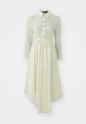 Vestuário de manga longa e gola em creme com bolinhas pretas. Apresenta uma frente com botão e cintura franzida com uma bainha fluida.