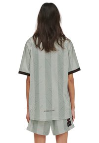 Ljusgrå oversize skjorta och shorts-set med ett geometriskt mönster, korta ärmar och en krage och fåll med röd accent.