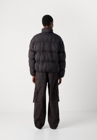 Svart boblejakke med høy krage, med en kviltet design og en skinnende tekstur, båret over mørke cargobukser med sidelommer.