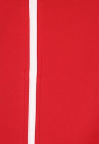 Un material textil roșu, cu o textură netedă, având o dublă bandă verticală albă proeminentă pe o latură. Cusăturile sunt vizibile.