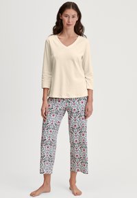 Licht beige V-hals top met driekwart mouwen, gecombineerd met pyjamabroek met bloemenprint in roze en groen op een witte achtergrond.