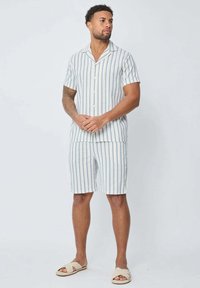 Ensemble de chemise à manches courtes rayée et de shorts en blanc, bleu clair et beige. Tissu léger, fermeture à boutons, coupe décontractée.