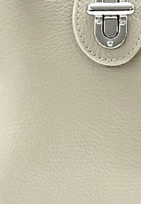 Beige leren handtas met een gladde textuur, voorzien van een zilverkleurige metalen sluiting en gestikte accenten, met een gestructureerd ontwerp.