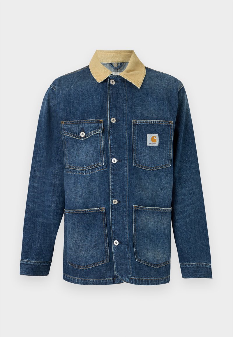 Blauwe denim werkjas met beige kraag, vier voorzakken, knoopsluiting en Carhartt-logo op de bovenste rechterzak.