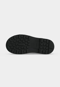 Semelle de chaussure en caoutchouc noir avec motifs de bande de roulement circulaires et rectangulaires, avec un petit logo embossé au centre.