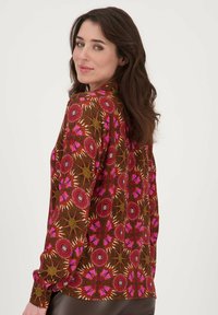 Langarige blouse van patroonstof in bruin, roze en oranje tinten. Heeft ronde motieven en knoopsluiting aan de manchetten.