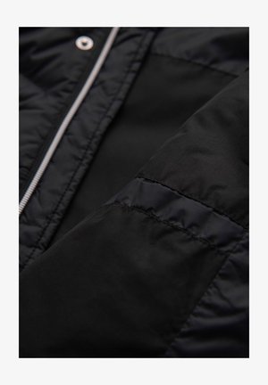 Czarna ocieplana kurtka z pikowanym wzorem, gładkim materiałem, srebrnym zamkiem błyskawicznym i zatrzaskami, z zblizeniem na rękaw i szwy.