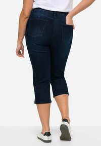 Pantaloni capri in denim scuro con vita aderente e gambe affusolate, dotati di due tasche posteriori e orli arrotolati per un look casual.