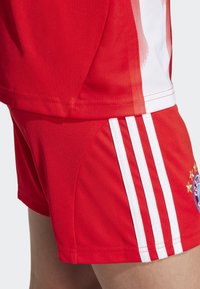 Červené atletické šortky s bielymi pruhmi a detailom loga, vyrobené z hladkej, ľahkej tkaniny. Obsahujú kontrastný dizajnový panel.