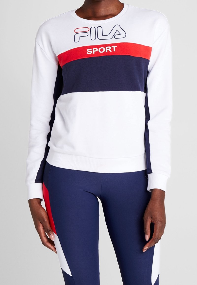 Bílá mikina s červenými a námořnickými horizontálními pruhy, s logem "FILA SPORT". V kombinaci s námořnickými legínami a kontrastními barevnými panely.