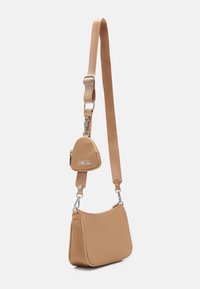Tan crossbody-väska med en böjd form, tillverkad av ett slätt material, med en avtagbar liten ficka och detaljer i silverfärg.