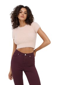 Maglione cropped rosa chiaro con maniche corte, texture morbida e pelosa. Abbinato a jeans skinny a vita alta di un profondo bordeaux.