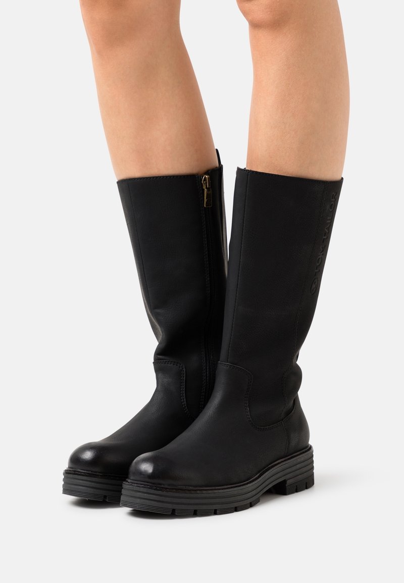 Bottes noires en cuir hauteur genoux, dotées d'une fermeture éclair sur le côté, d'une surface texturée et d'une semelle crantée pour la traction. Marque visible sur le tige.