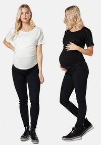 Maternity tops in white and black, featuring short sleeves and a fitted design. Black pants and ankle boots complete the outfits.