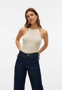 Body di colore crema lavorato a maglia con scollatura a onde, abbinato a jeans in denim blu scuro a vita alta con bottone frontale e tasche.