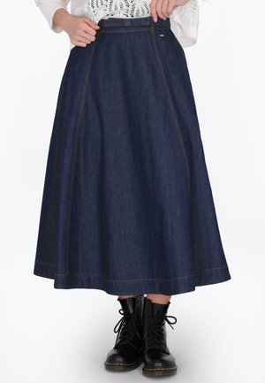 Femme portant une jupe trapèze en denim foncé à taille haute avec des détails de couture à l'avant et des bottines noires à lacets.